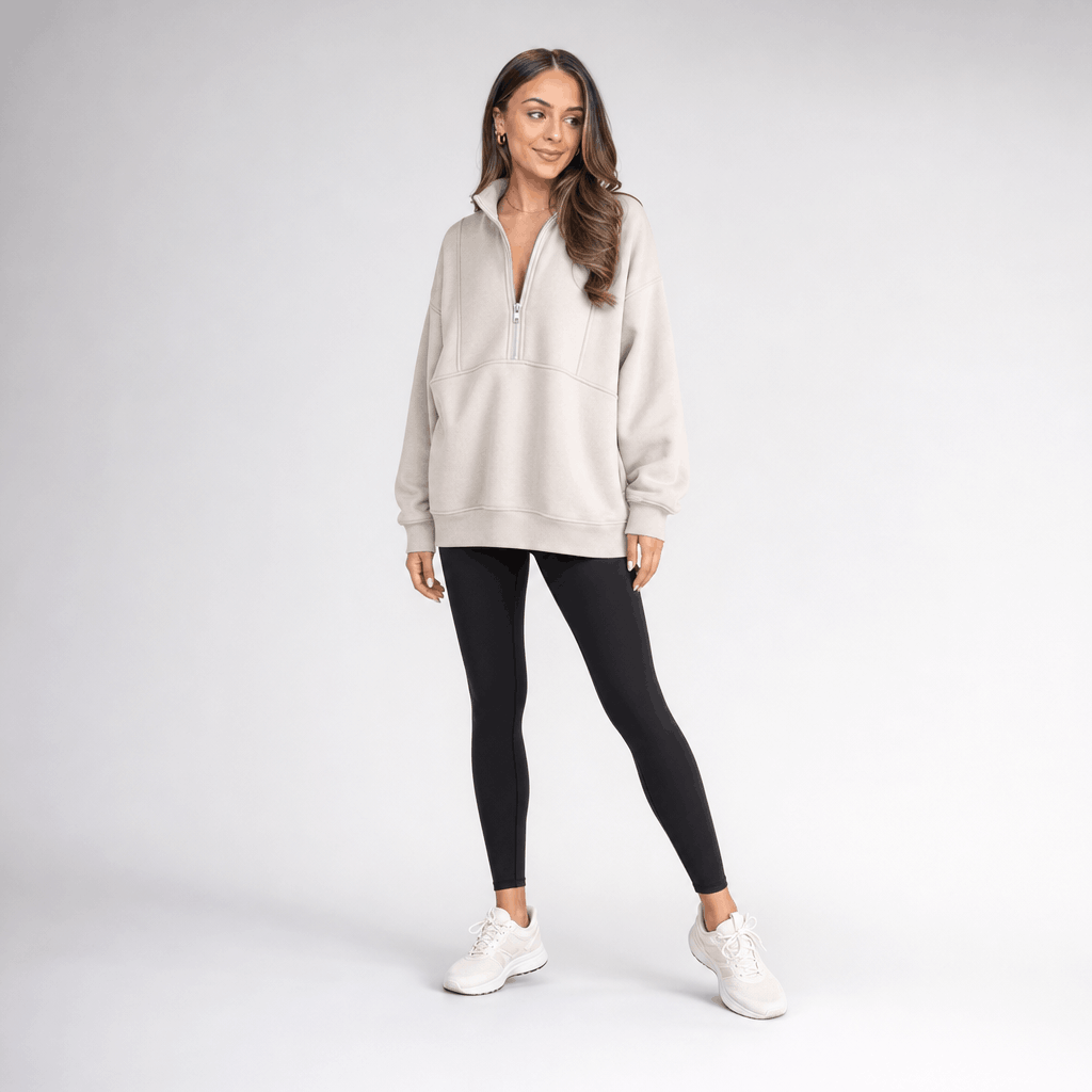 Full-body view of a female model wearing the beige quarter-zip pullover with black trousers and white sneakers.