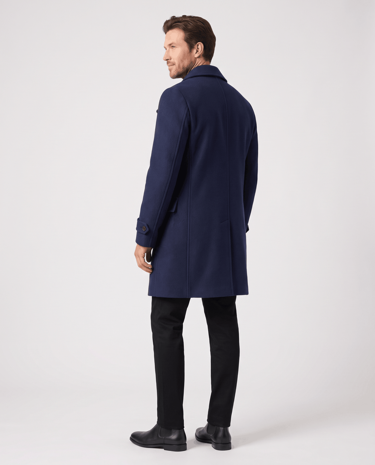 Back view of a long navy blue wool coat with black trousers and boots
