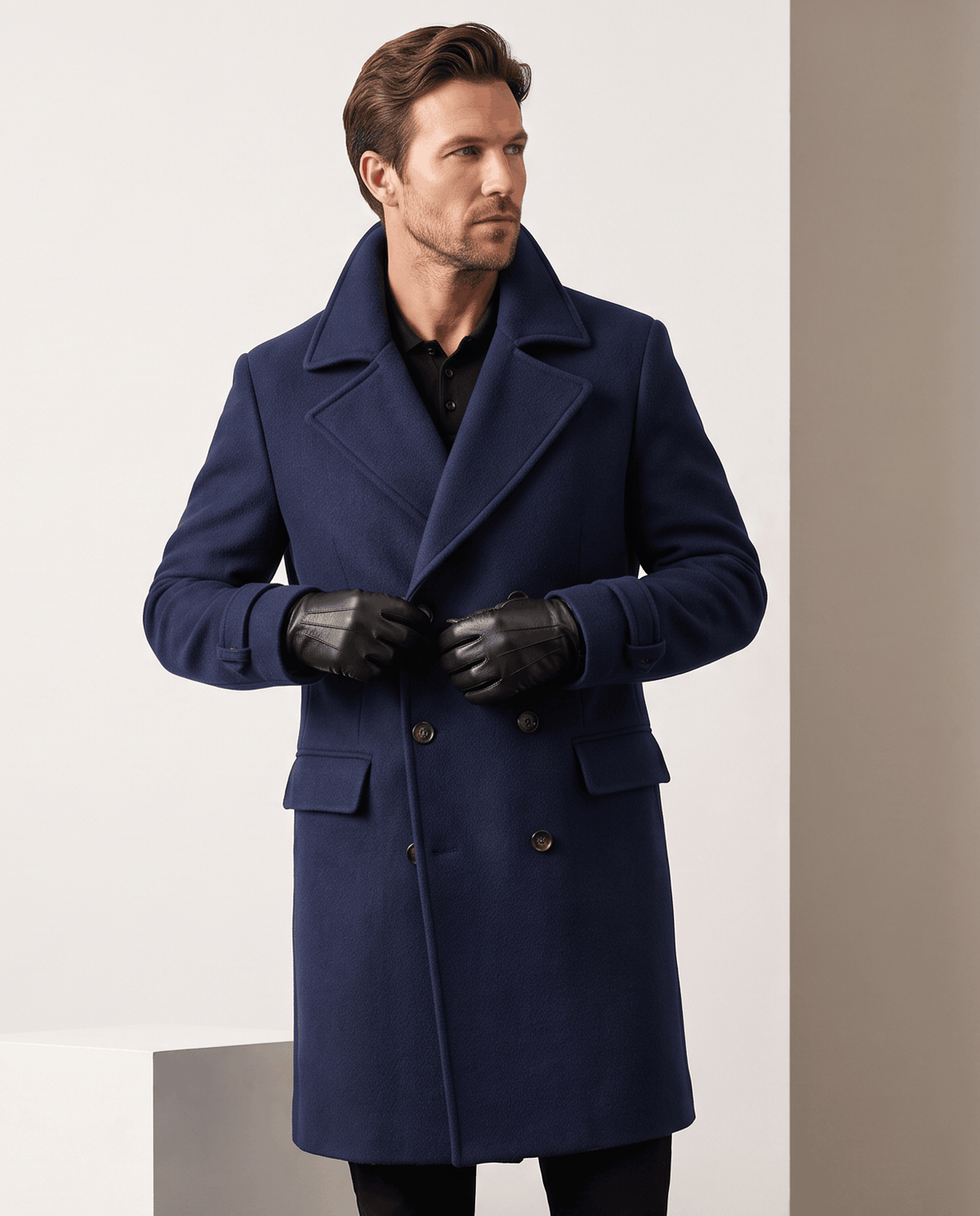Man wearing a navy blue double-breasted wool coat with flap pockets and black leather gloves