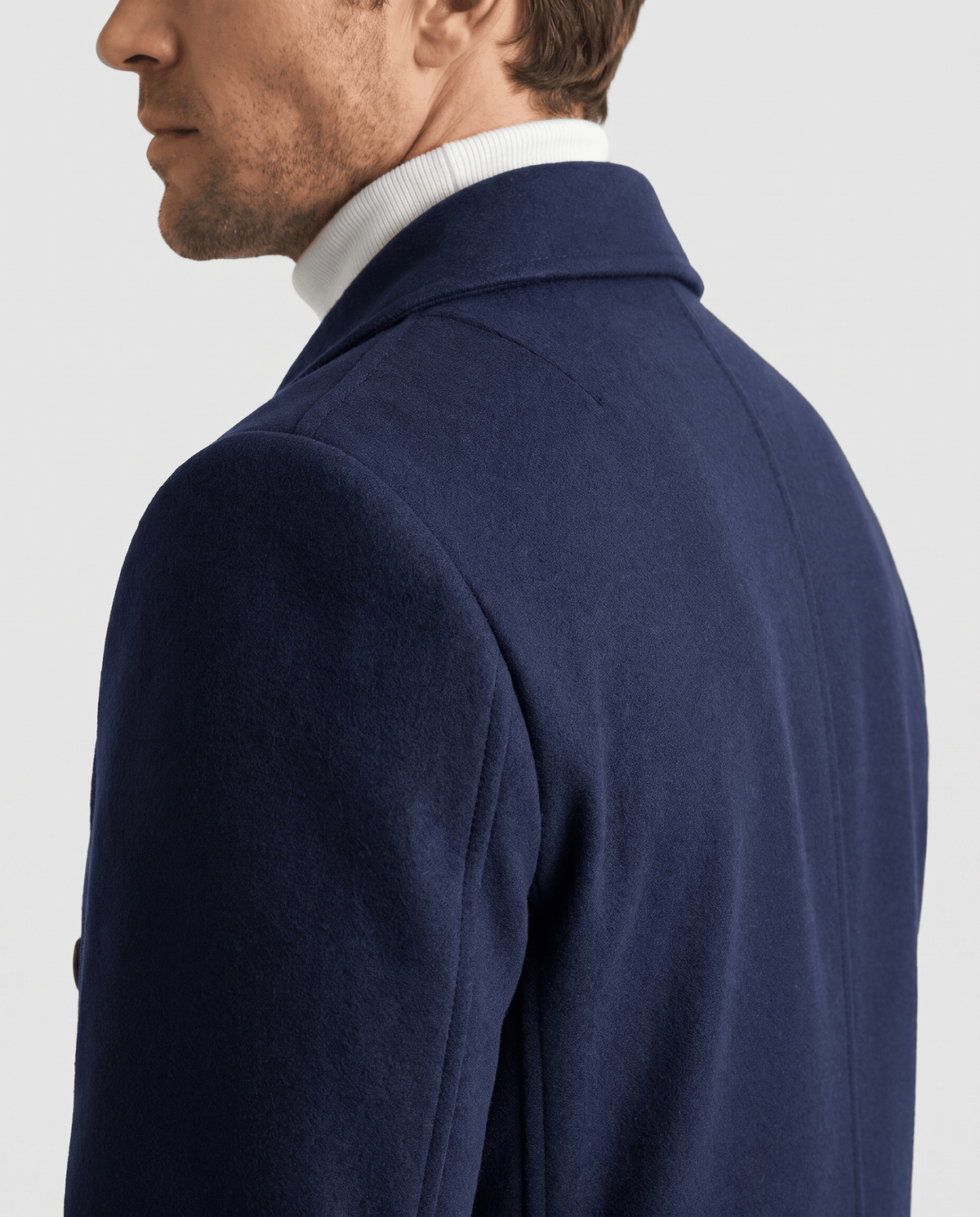 Close-up of a navy blue wool coat shoulder and collar worn over a white turtleneck