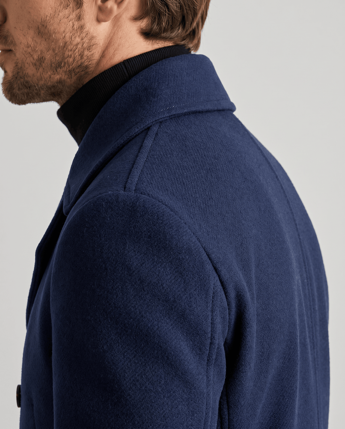 Shoulder and collar detail of a navy blue wool coat over a black turtleneck
