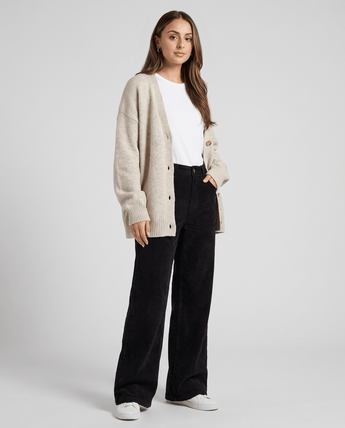 Model in black ribbed trousers styled with a cream cardigan and white sneakers