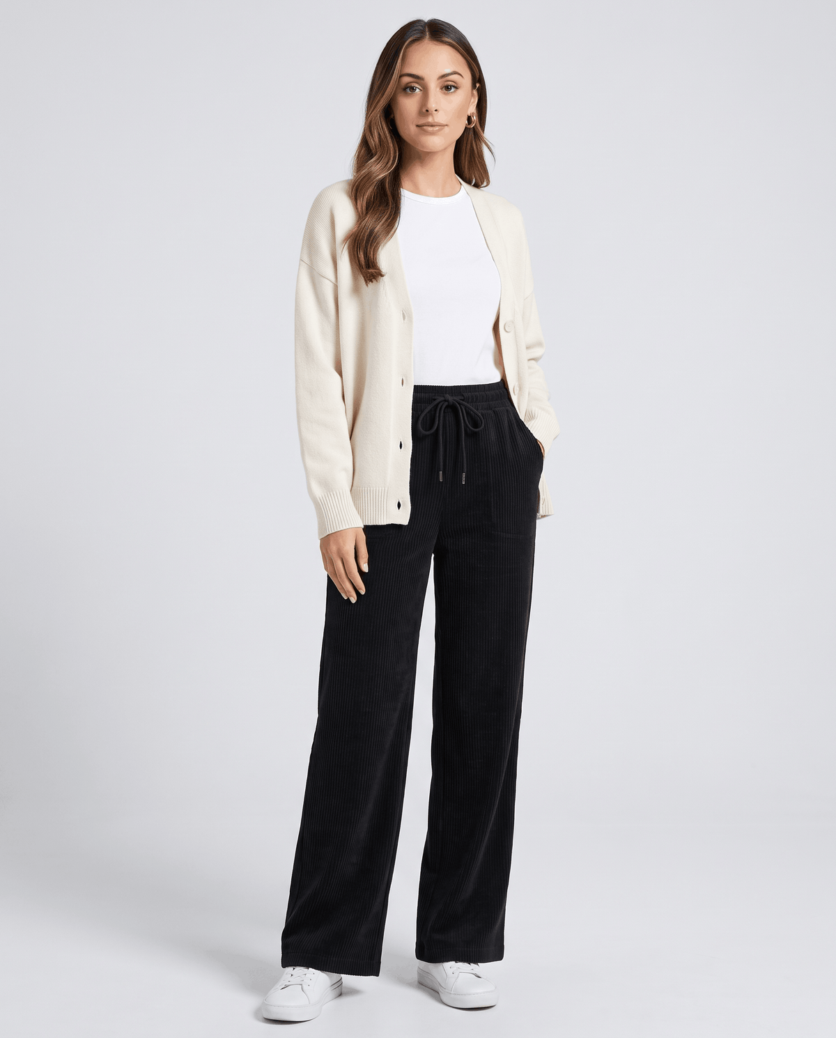 Model in black ribbed pants styled with a cream cardigan, white tee and white sneakers