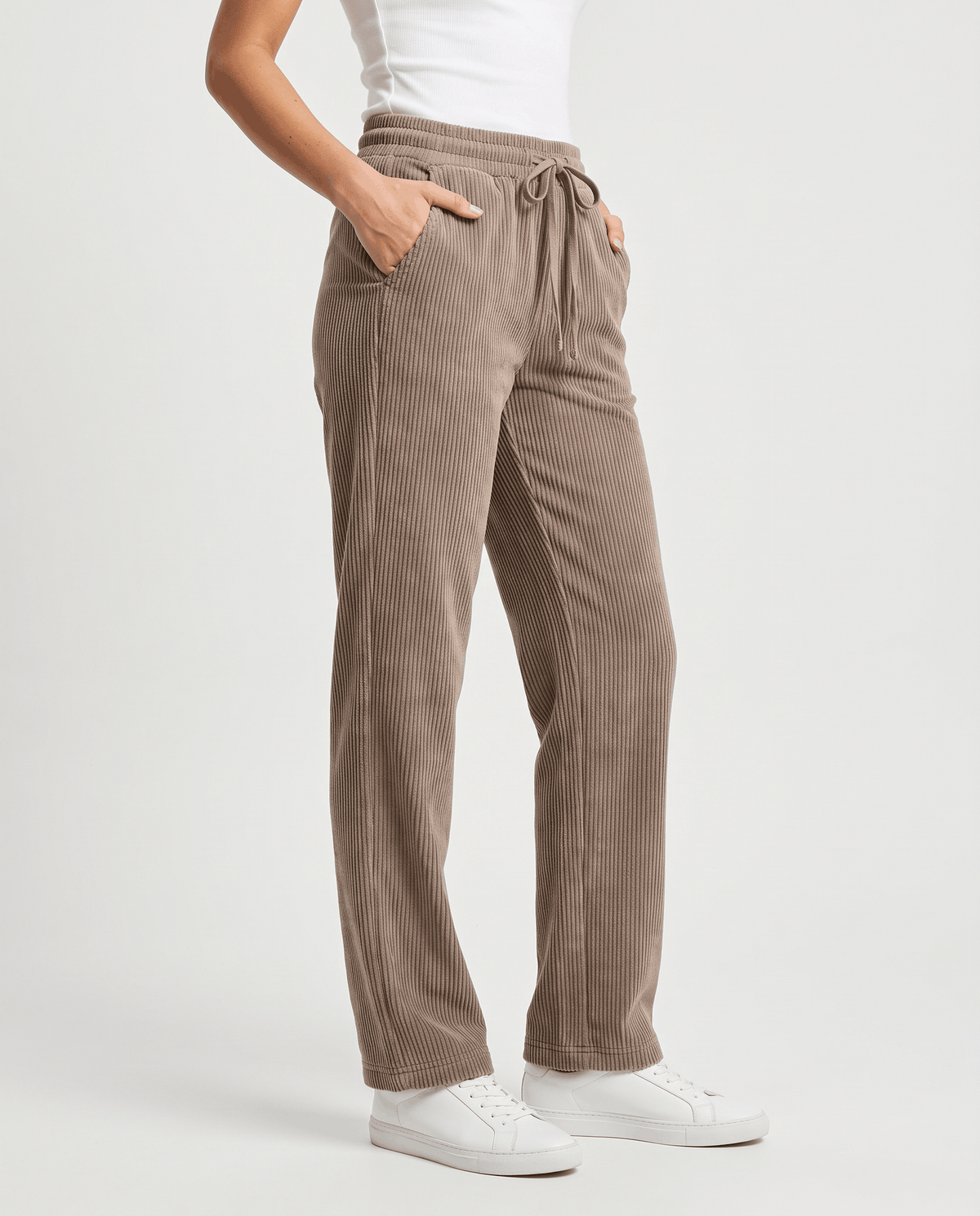 Front angled view of taupe corduroy pants with a tied drawstring and white sneakers
