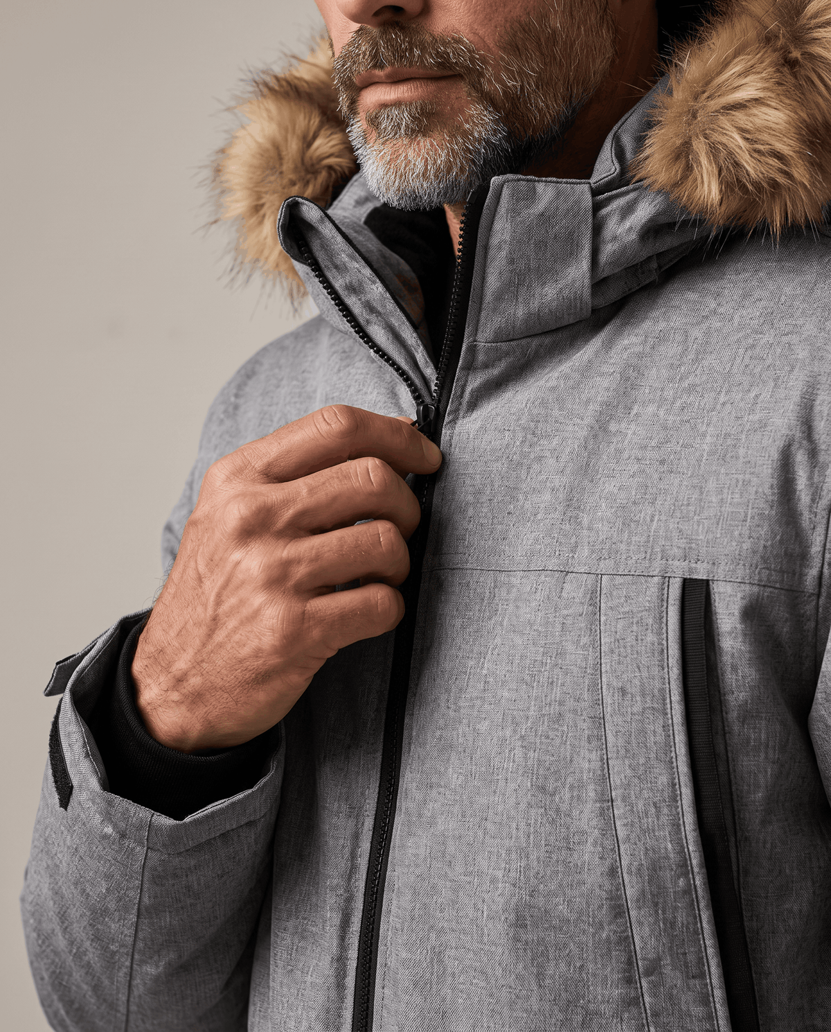 Man adjusting the zipped collar of a gray parka with a fur-trim hood