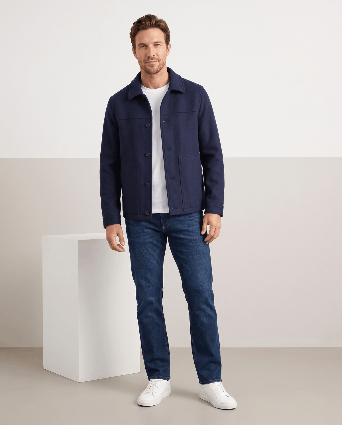 Model in a navy jacket and light jeans seated on a pale block