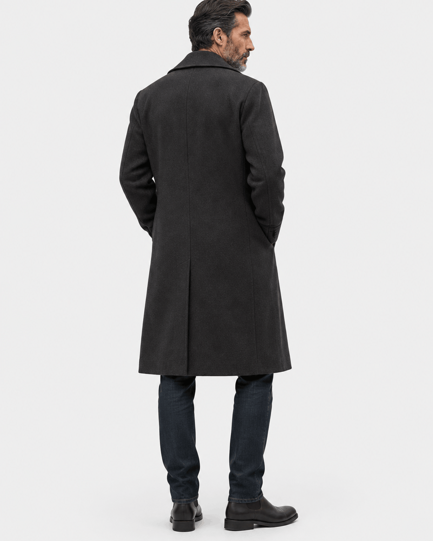 Back of the black long overcoat showing the clean shoulders and length with jeans and boots