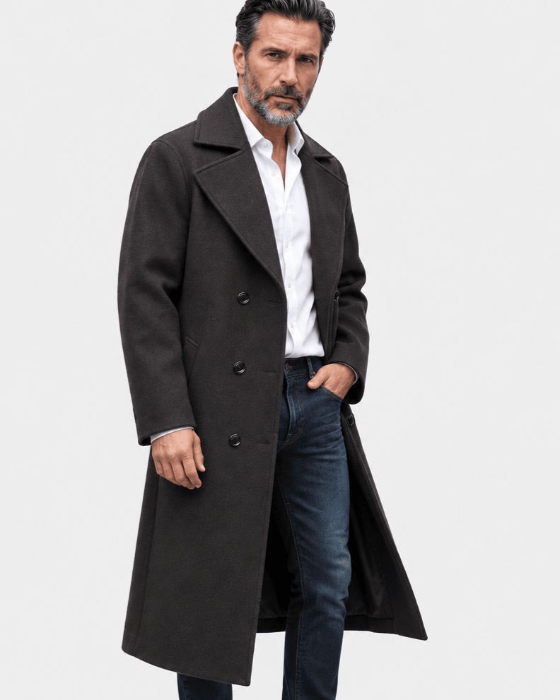 Black long overcoat in a three-quarter view with a white shirt, jeans and one hand in a pocket