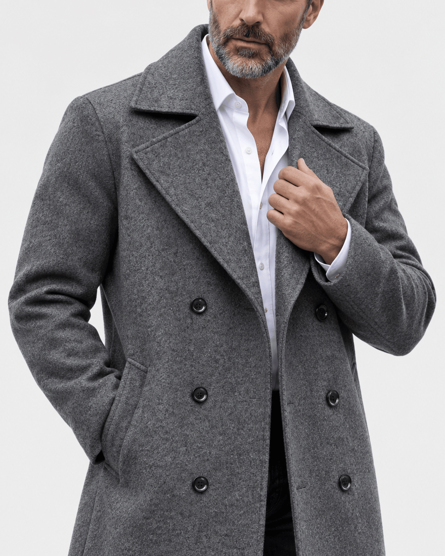 Close-up of the dark gray coat's textured fabric, wide lapel and buttons with a hand at the collar