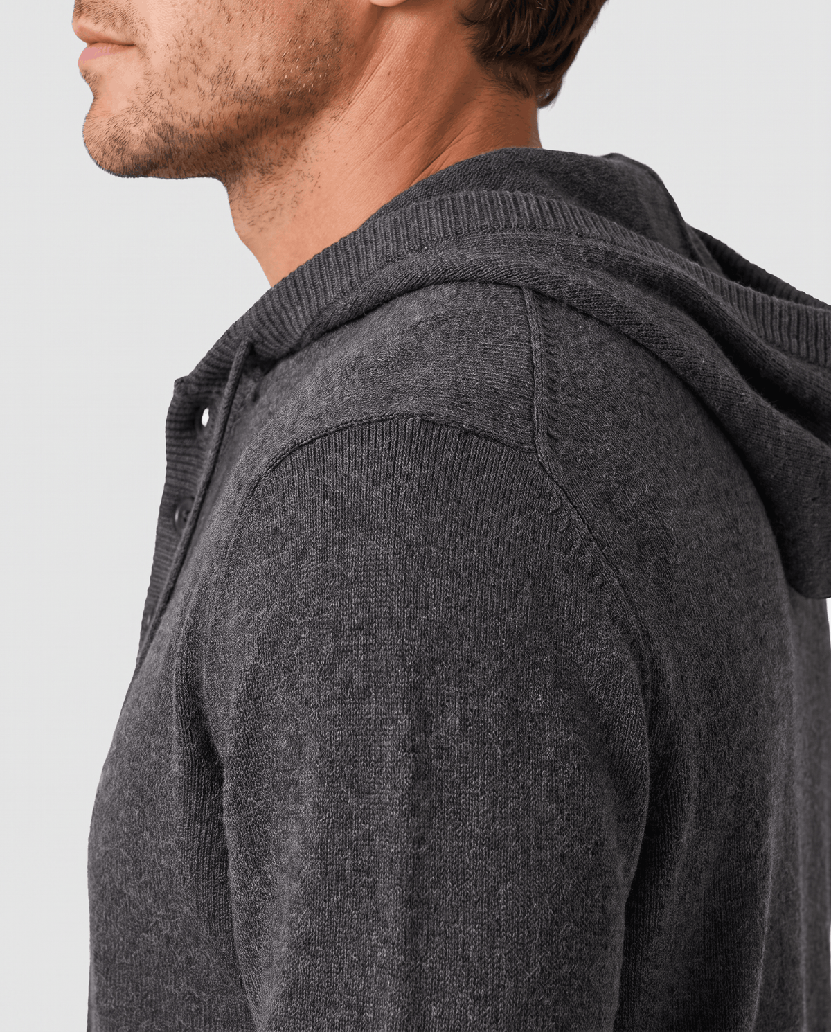 Side profile of a dark gray knit hoodie showing the hood and sleeve