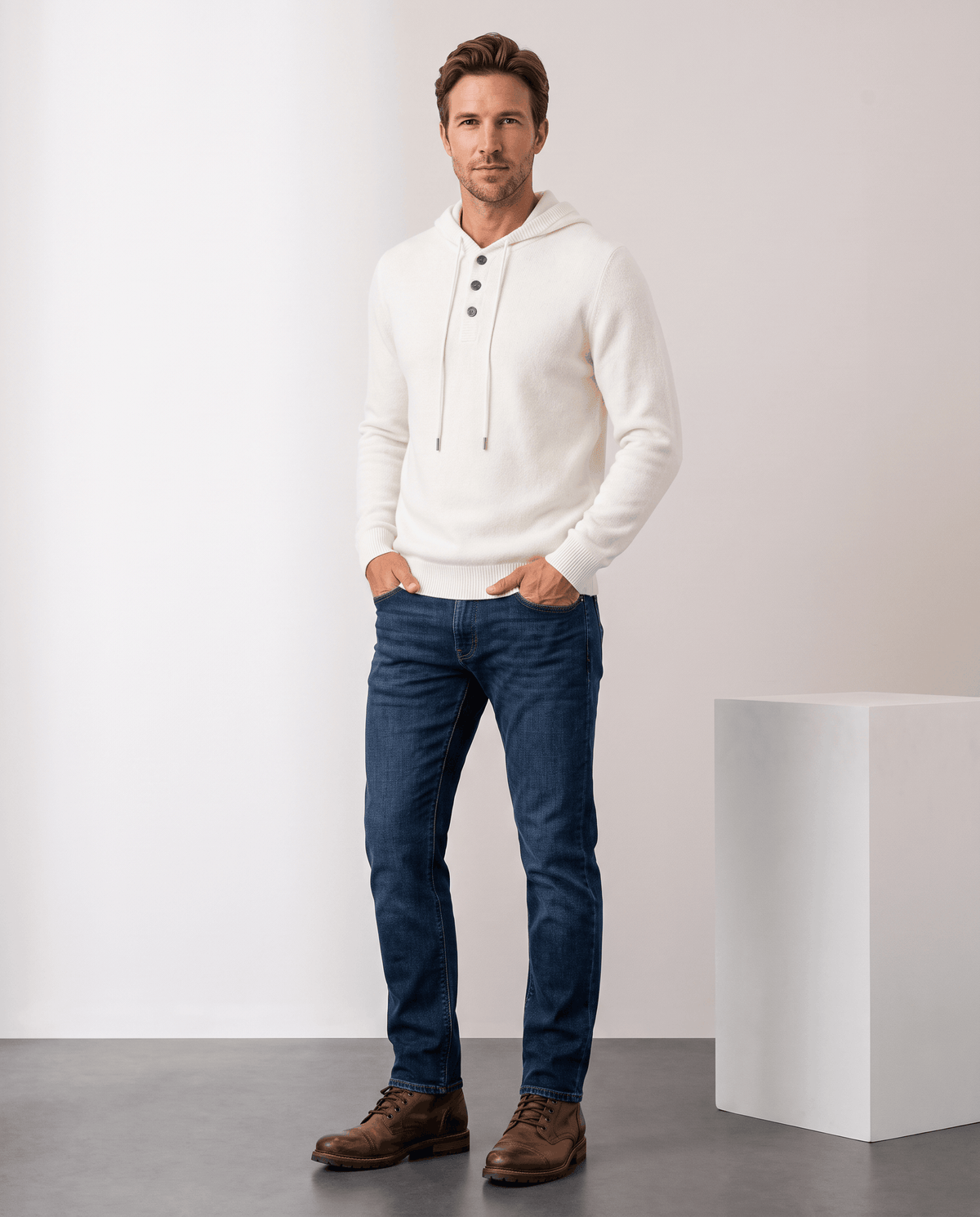 Full-length view of a man in an ivory knit hoodie, dark jeans and brown boots