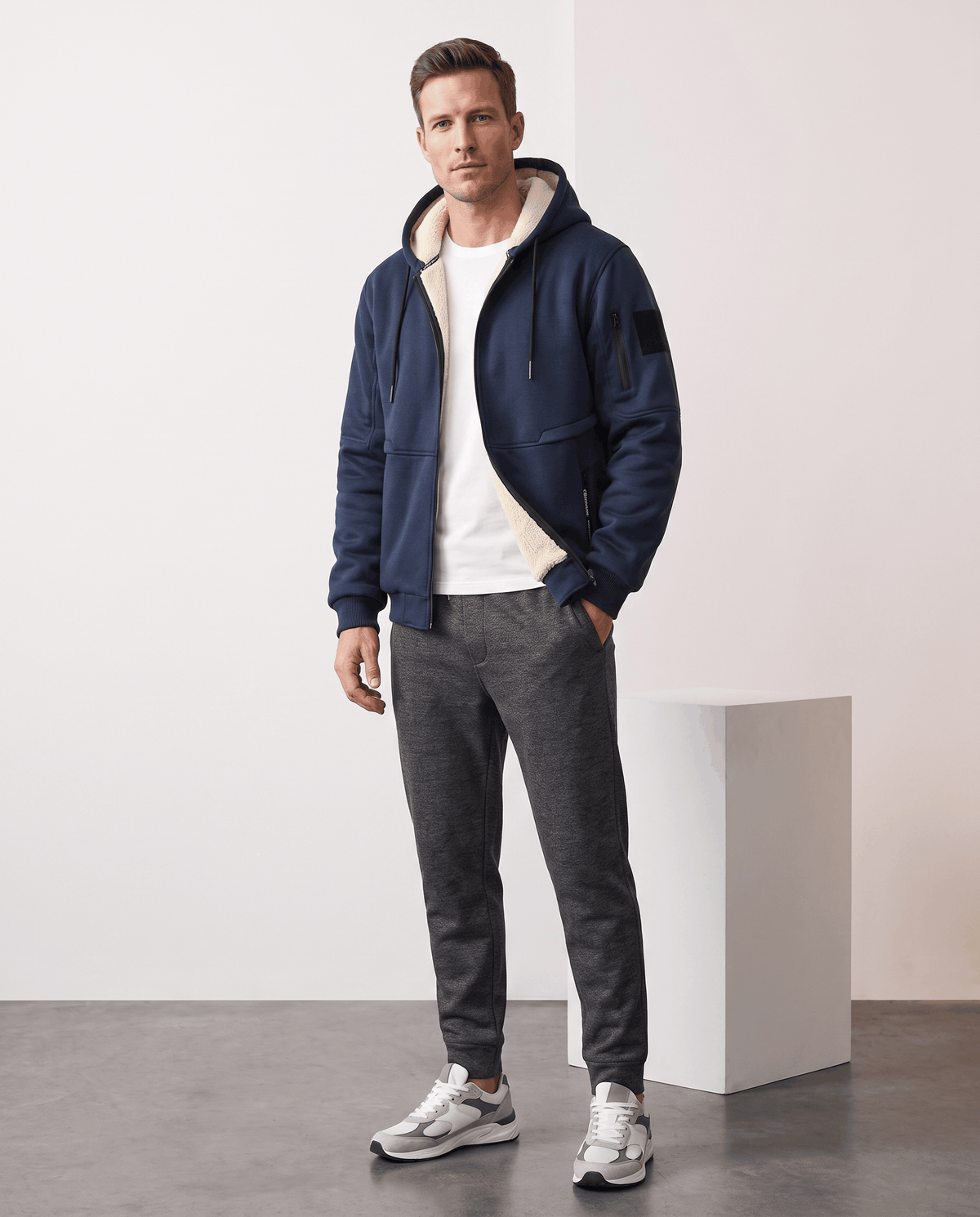 Full-length view of navy blue hooded jacket styled with dark gray pants and sneakers