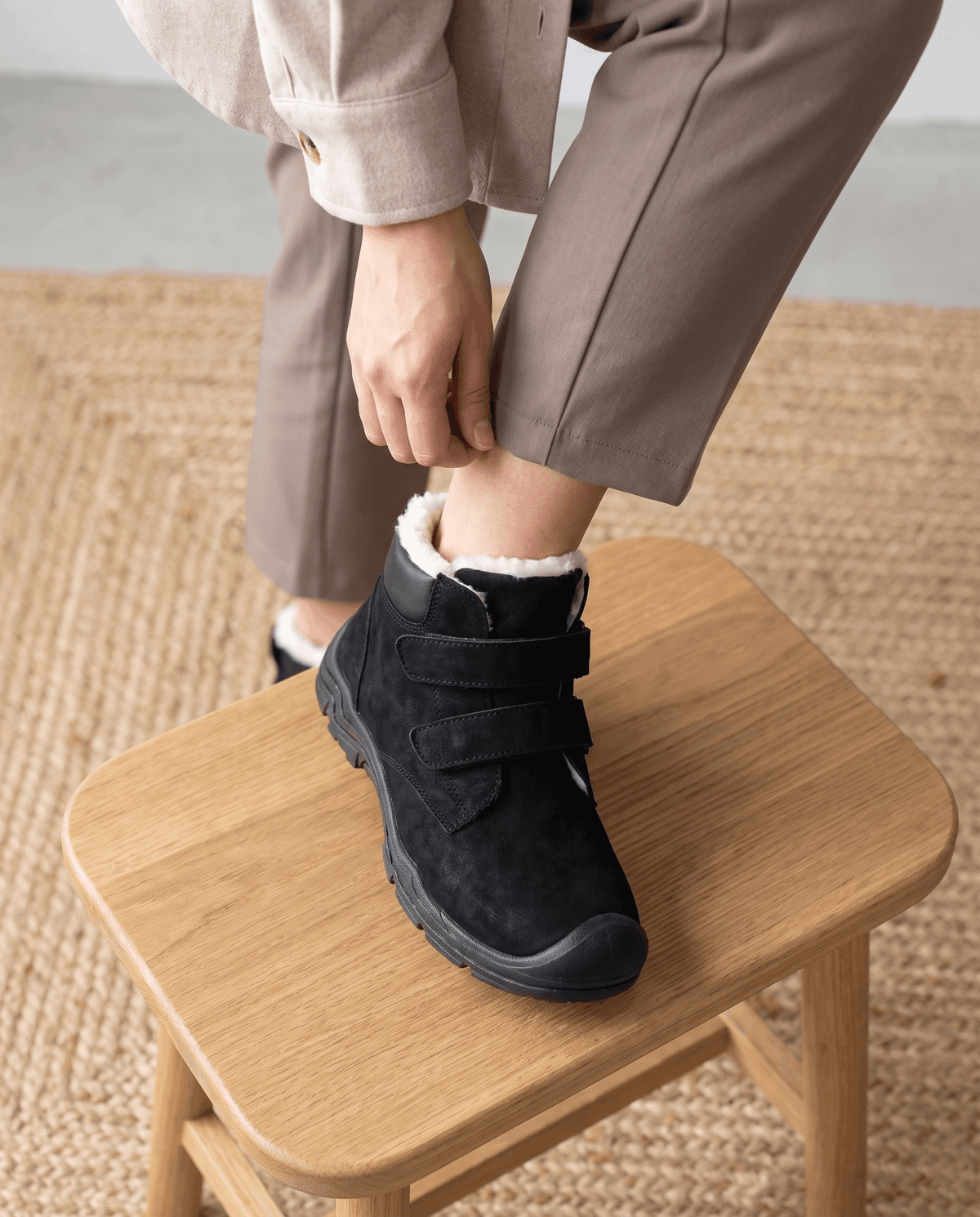 Person wearing black insulated boots while standing on a wooden stool.
