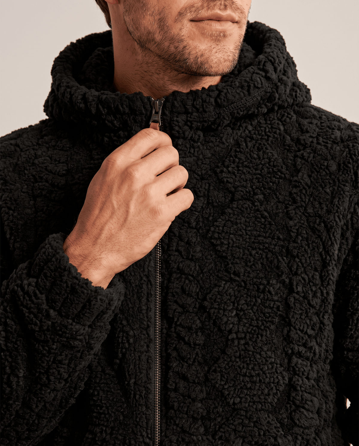 Close-up of black jacket zip and hood with a hand on the zip pull