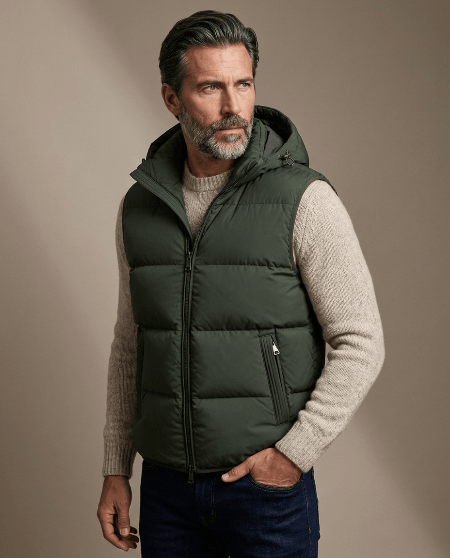 Men's hooded puffer vest in green worn over a cream sweater, hand in pocket