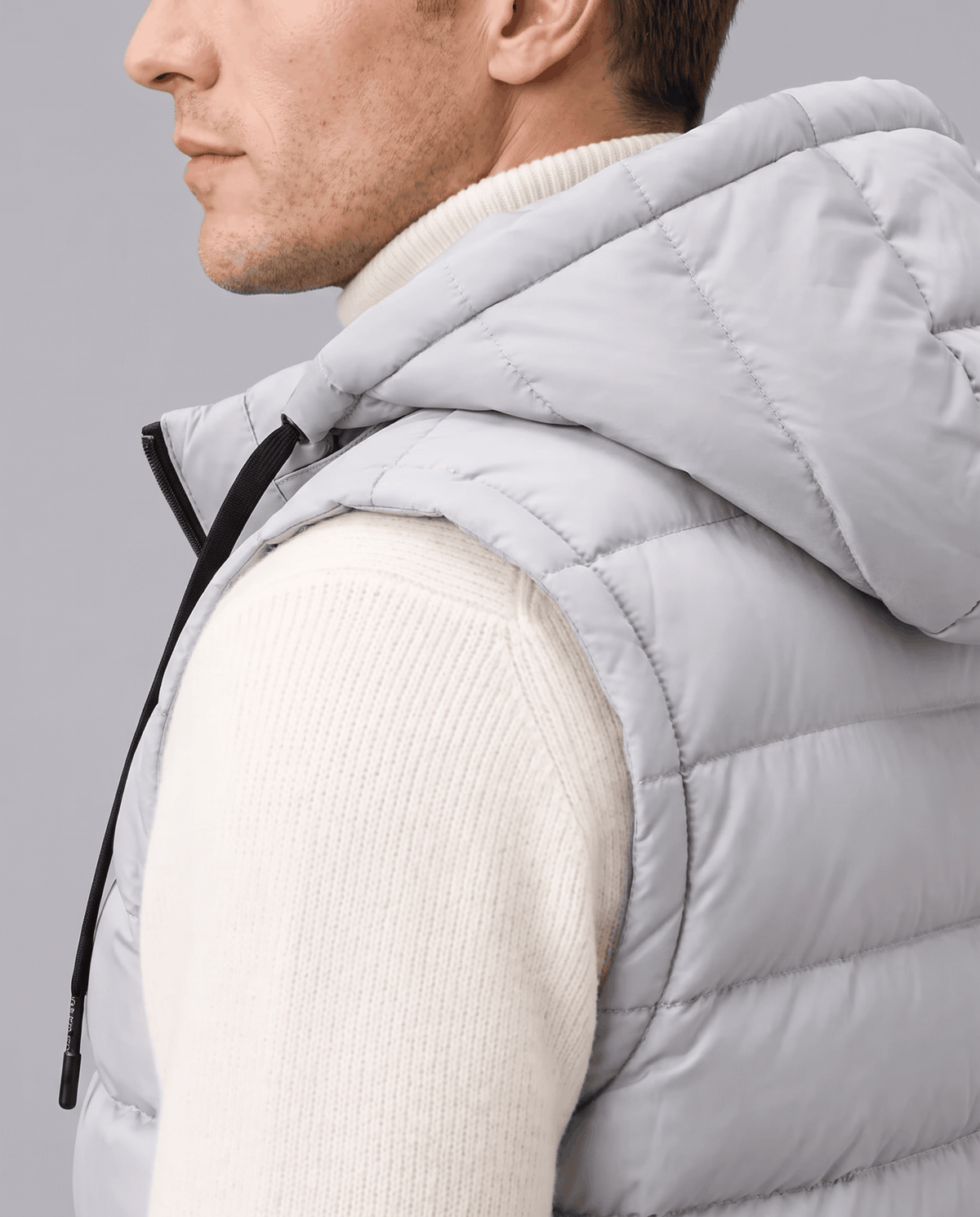 Side close-up of gray vest showing the hood and high collar over a cream sweater