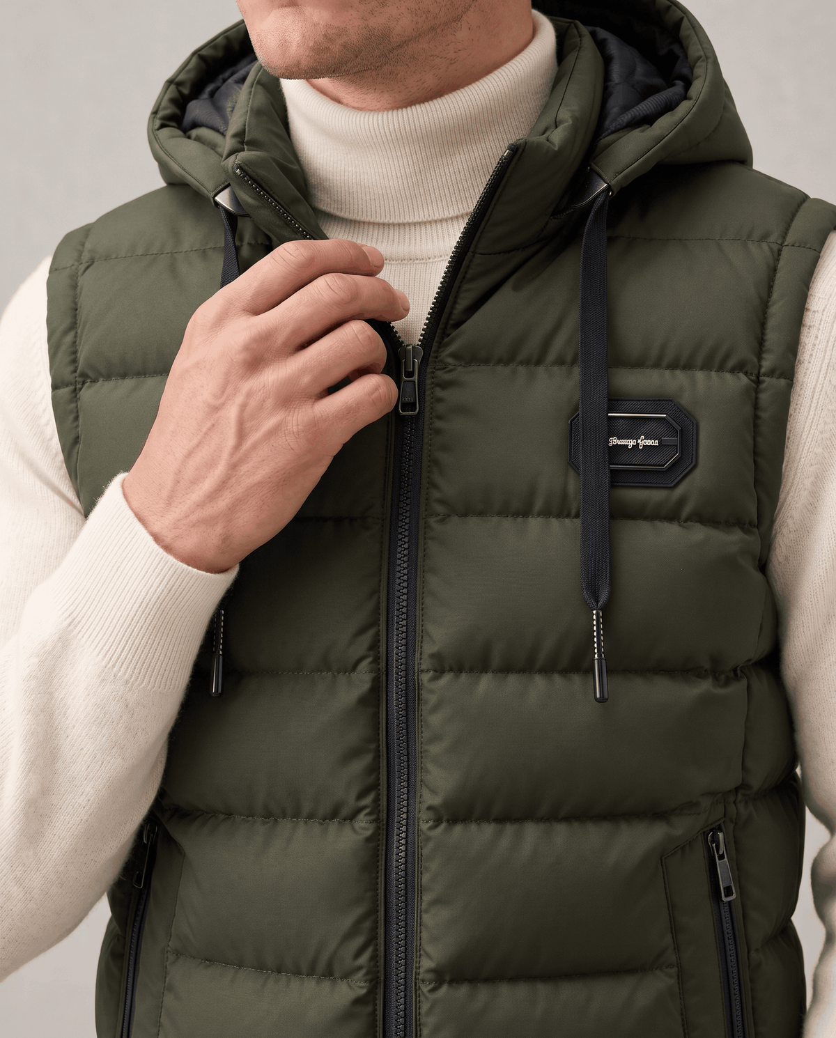 Close-up of green vest showing drawstring hood, chest badge, front zip and zip pocket