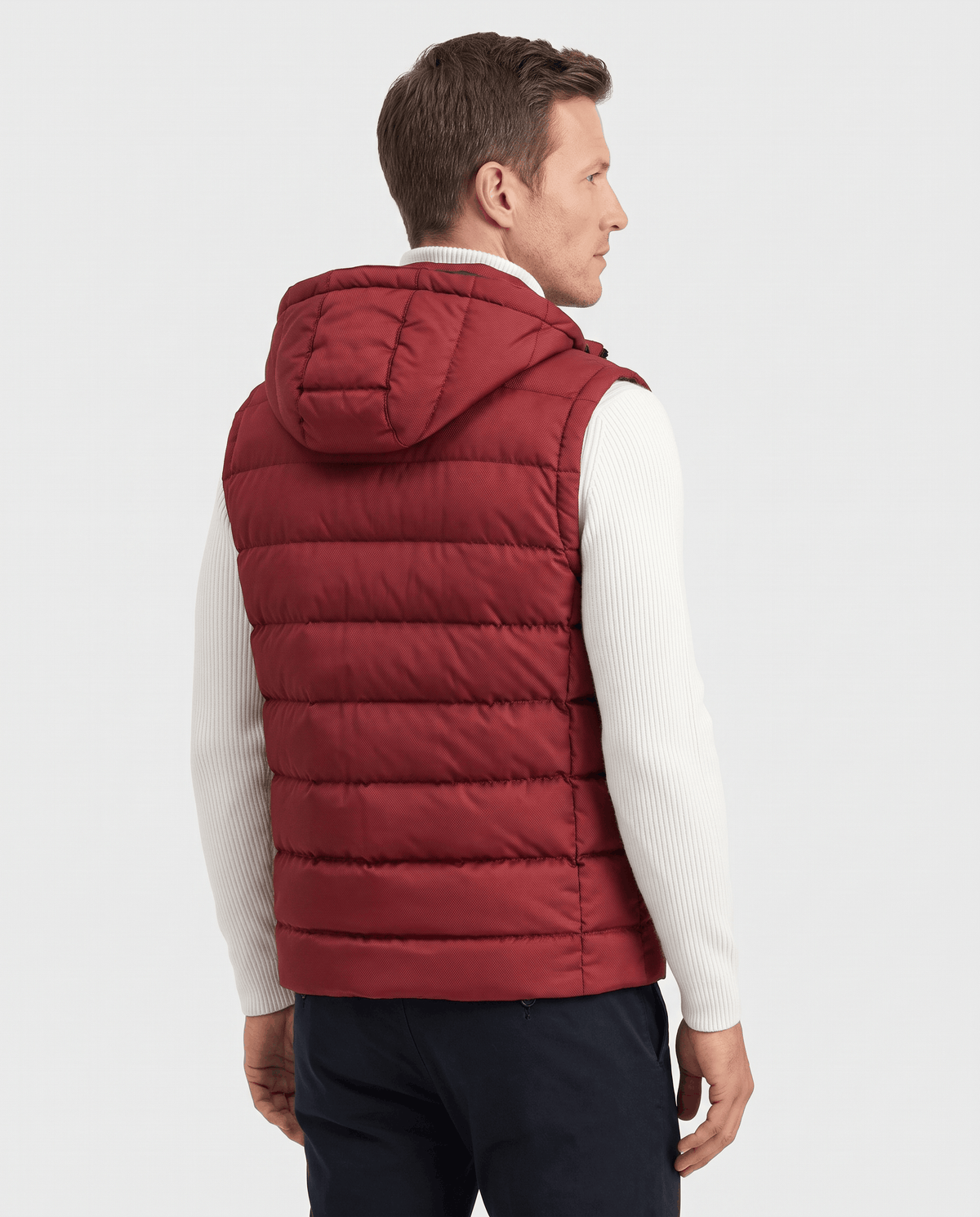 Back view of red hooded quilted vest over a white sweater and navy trousers