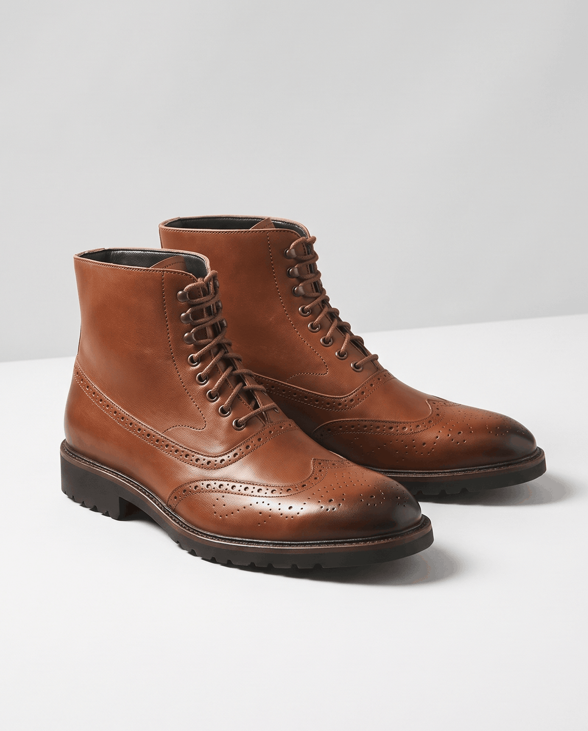 Pair of brown lace-up brogue ankle boots with dark soles on a light studio background