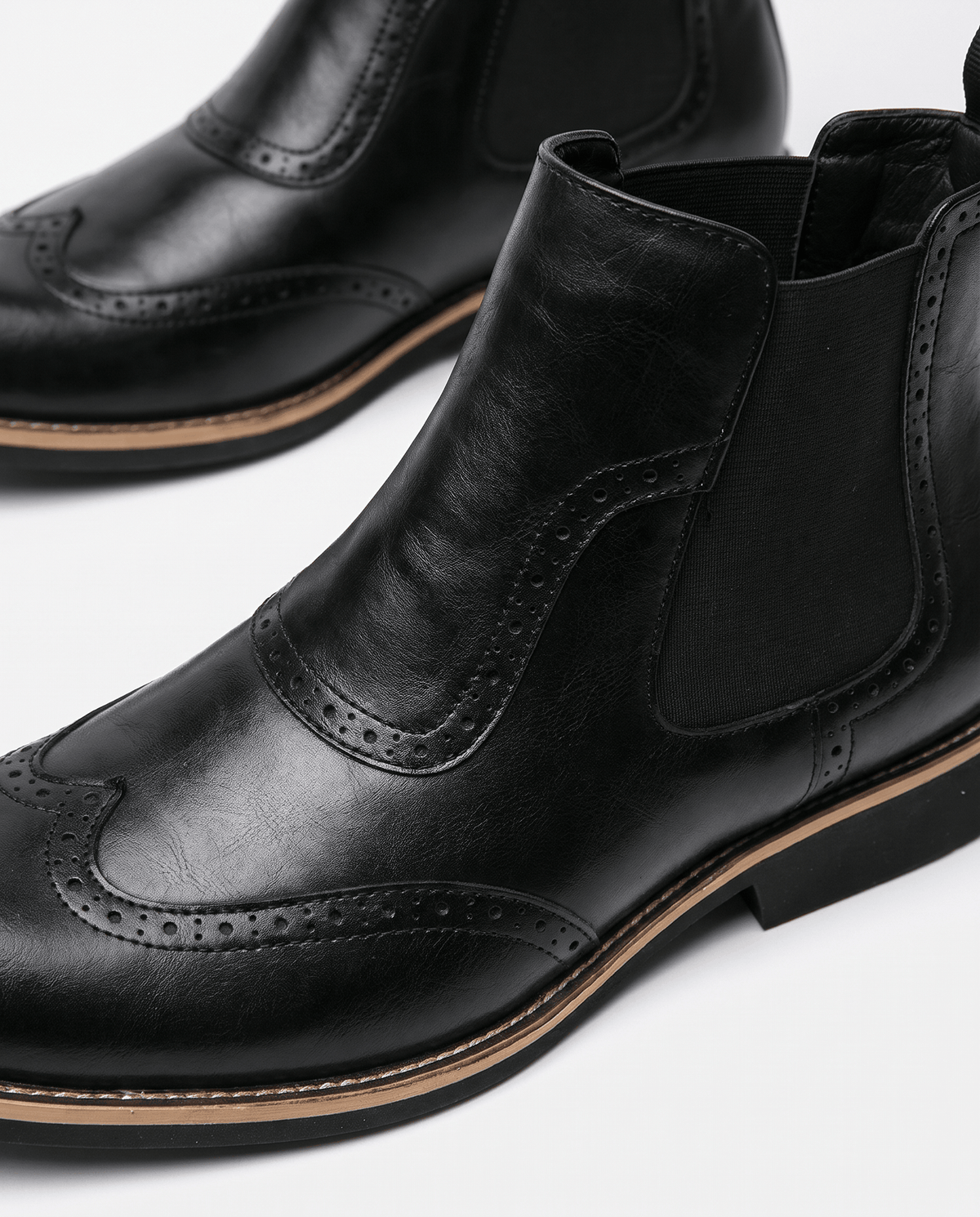 Close-up of black brogue toe perforations and elastic side panel on a Chelsea boot