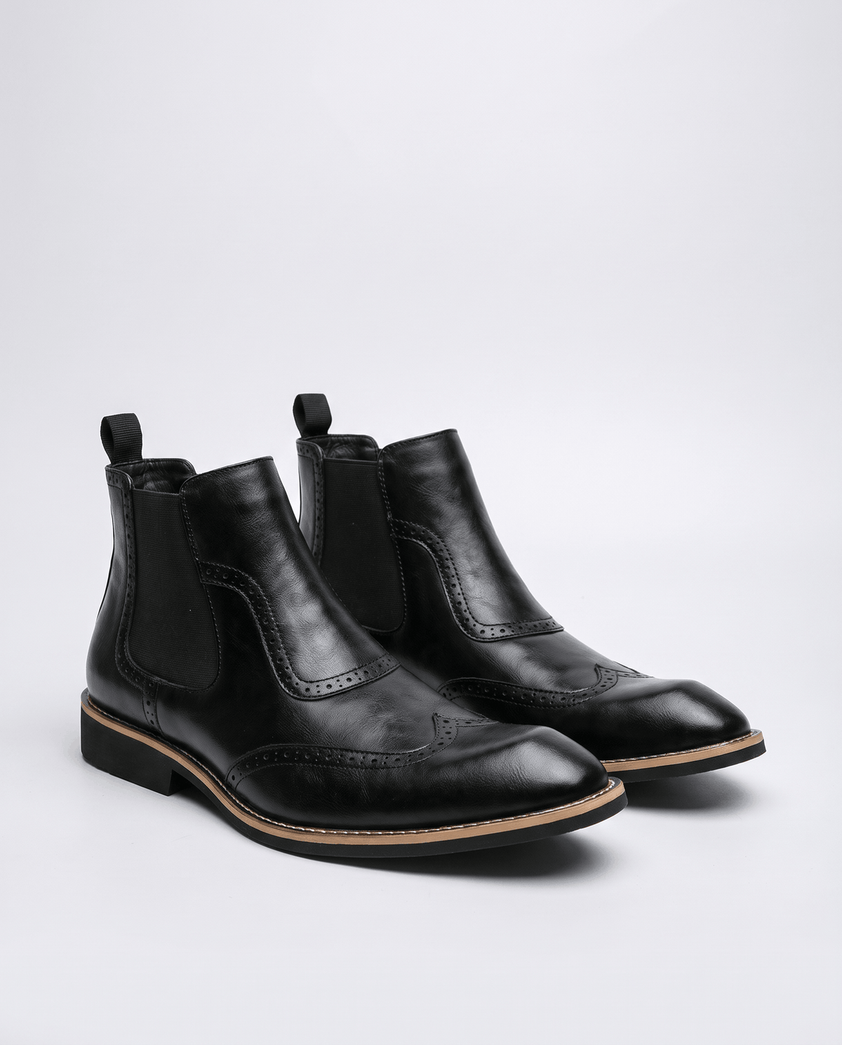 Pair of black slip-on brogue boots on a light studio background
