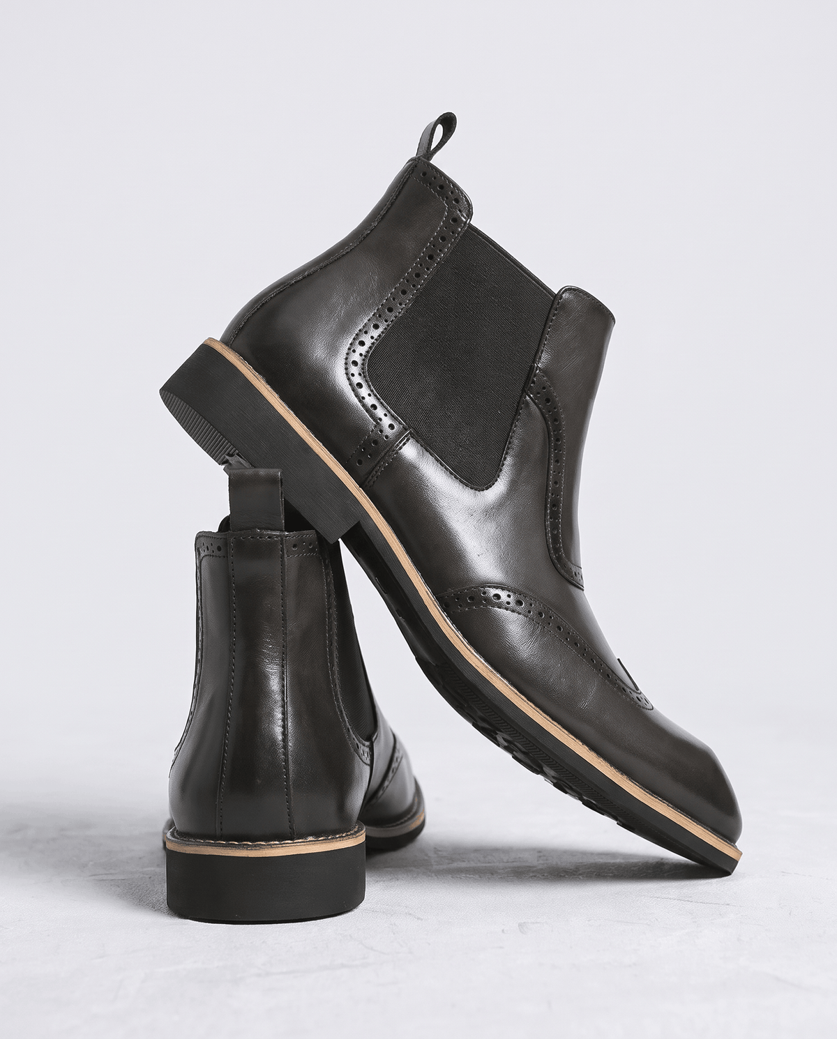 Black brogue boot tilted to show the rubber outsole, with a second boot beside it