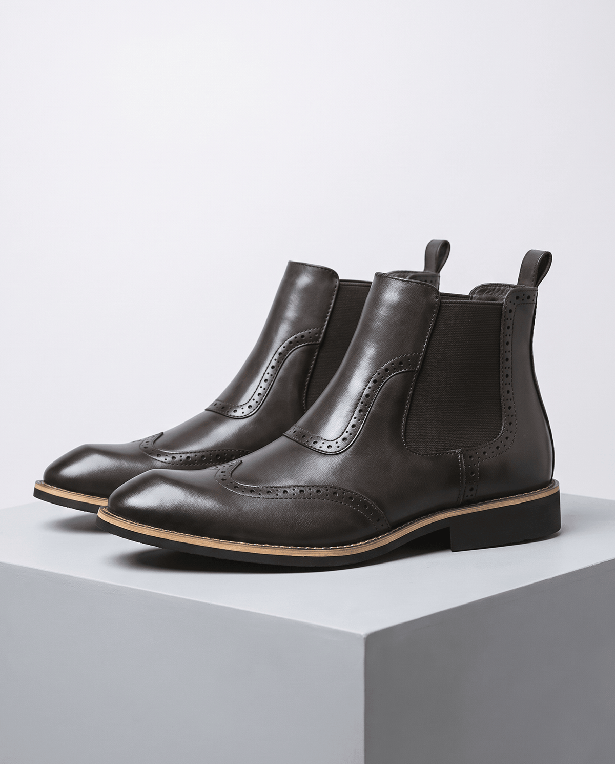 Pair of dark brown brogue Chelsea boots on a gray block