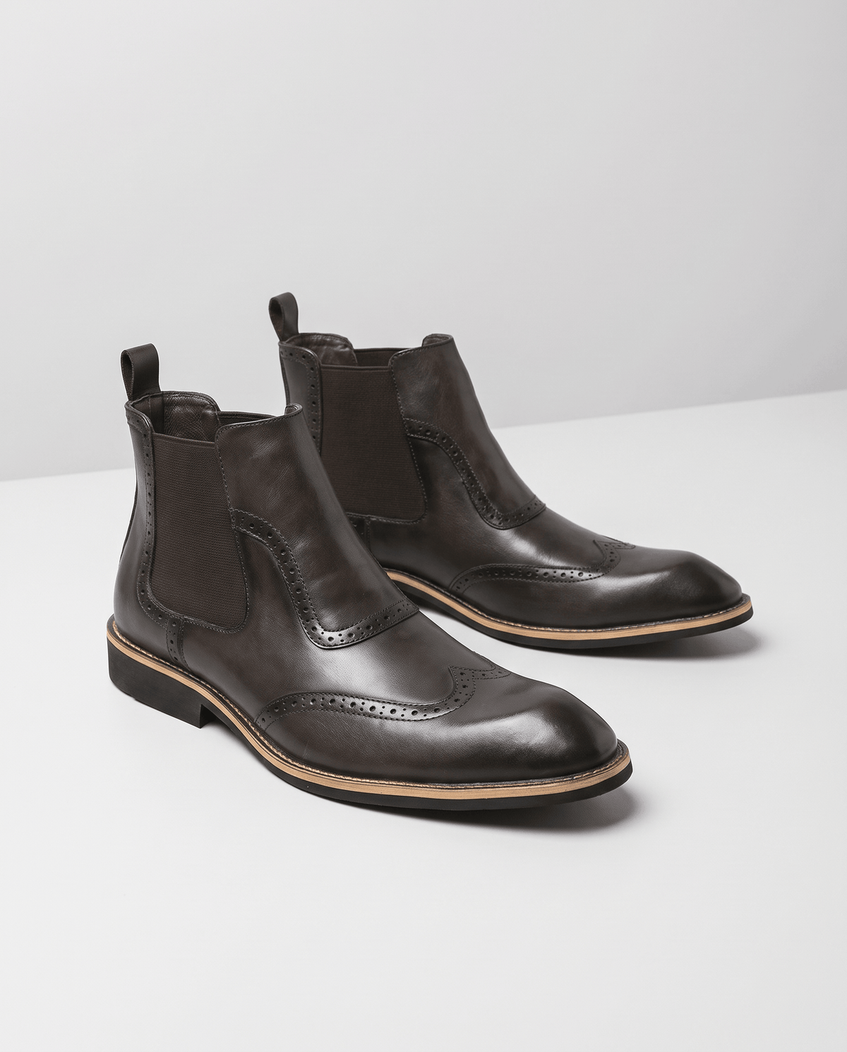 Dark brown slip-on brogue boots shown as a pair on a light surface