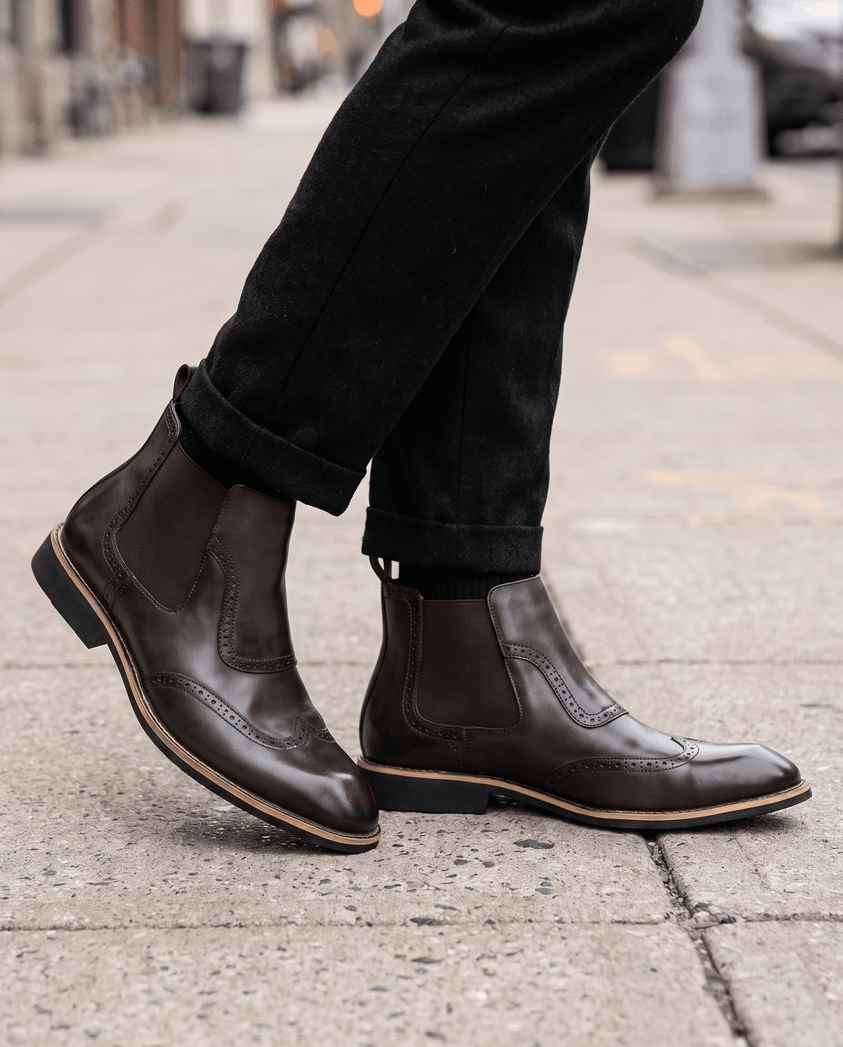 Man in dark brown slip-on brogue boots and black trousers on a tiled pavement
