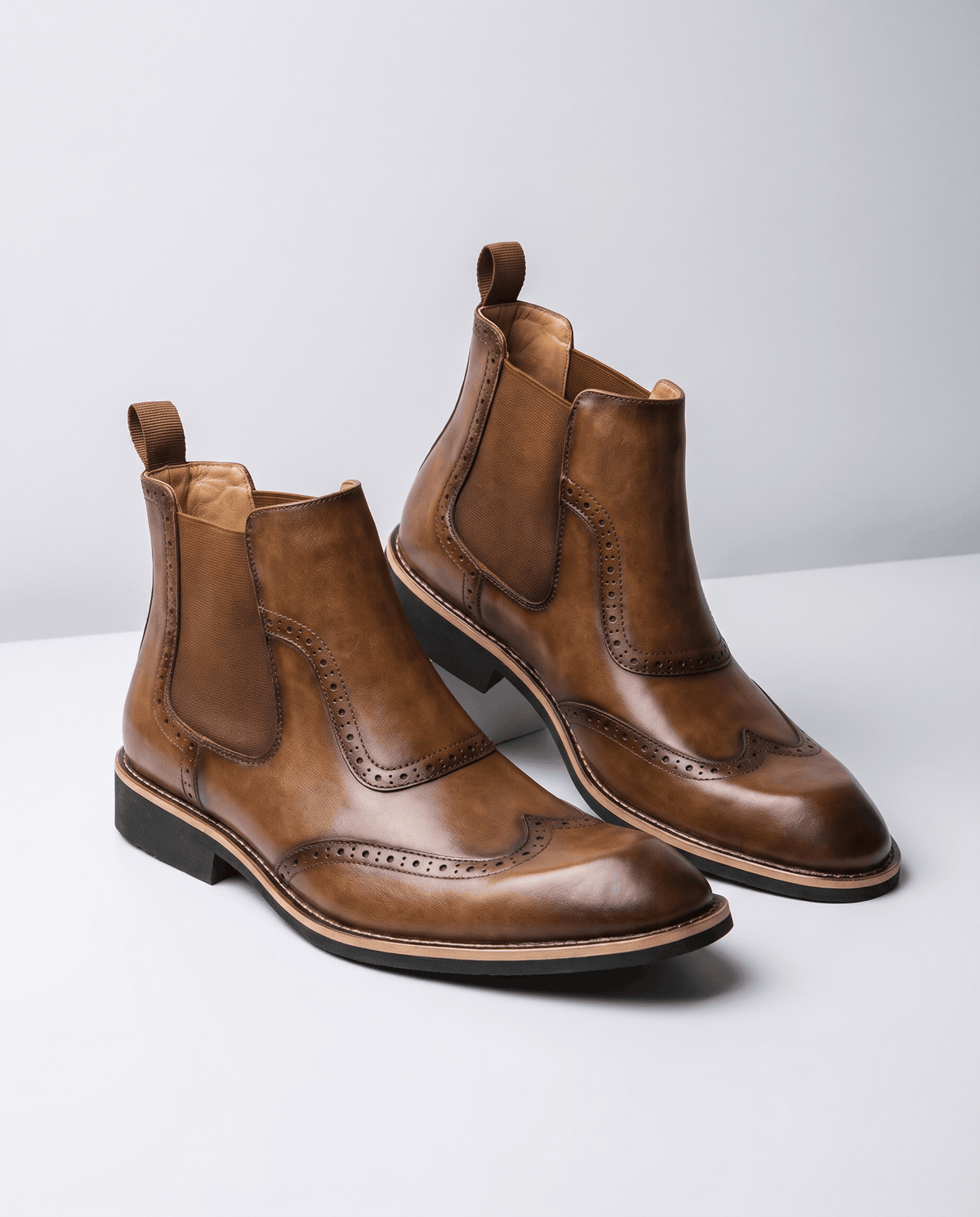 Tan slip-on boots with brogue toe detailing angled on a light surface