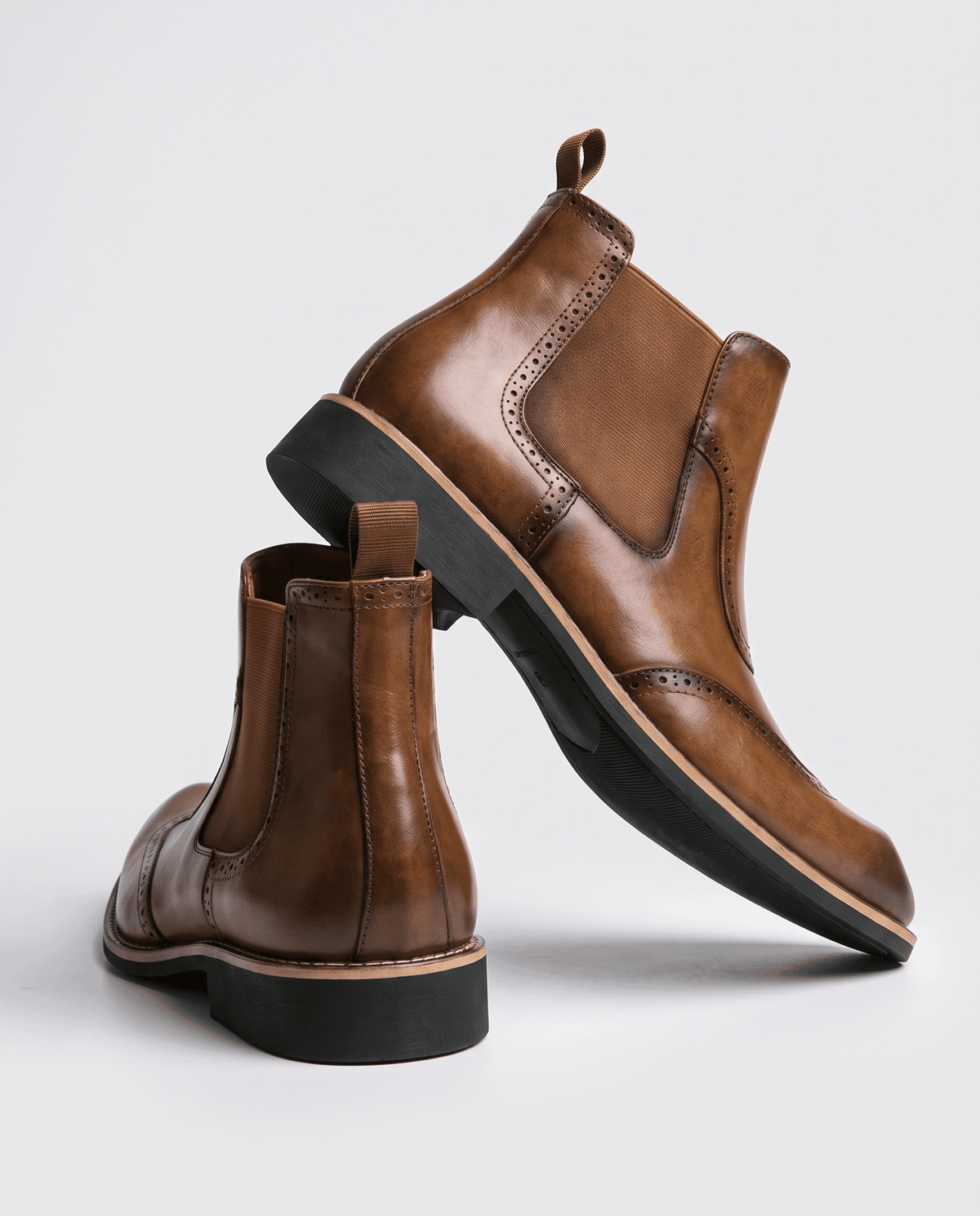 Tan brogue boot tilted to show the outsole, with a second boot standing behind