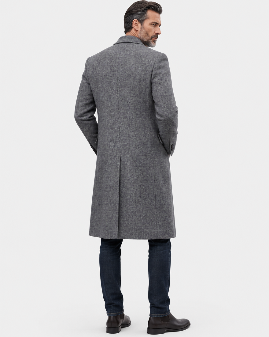 Back of the gray long overcoat showing a center vent and straight hem over dark trousers and shoes