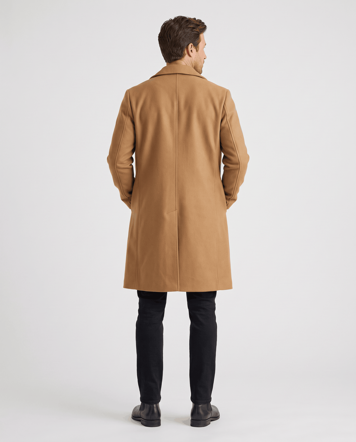 Back of the brown longline coat with a center vent, worn with black trousers and dark shoes