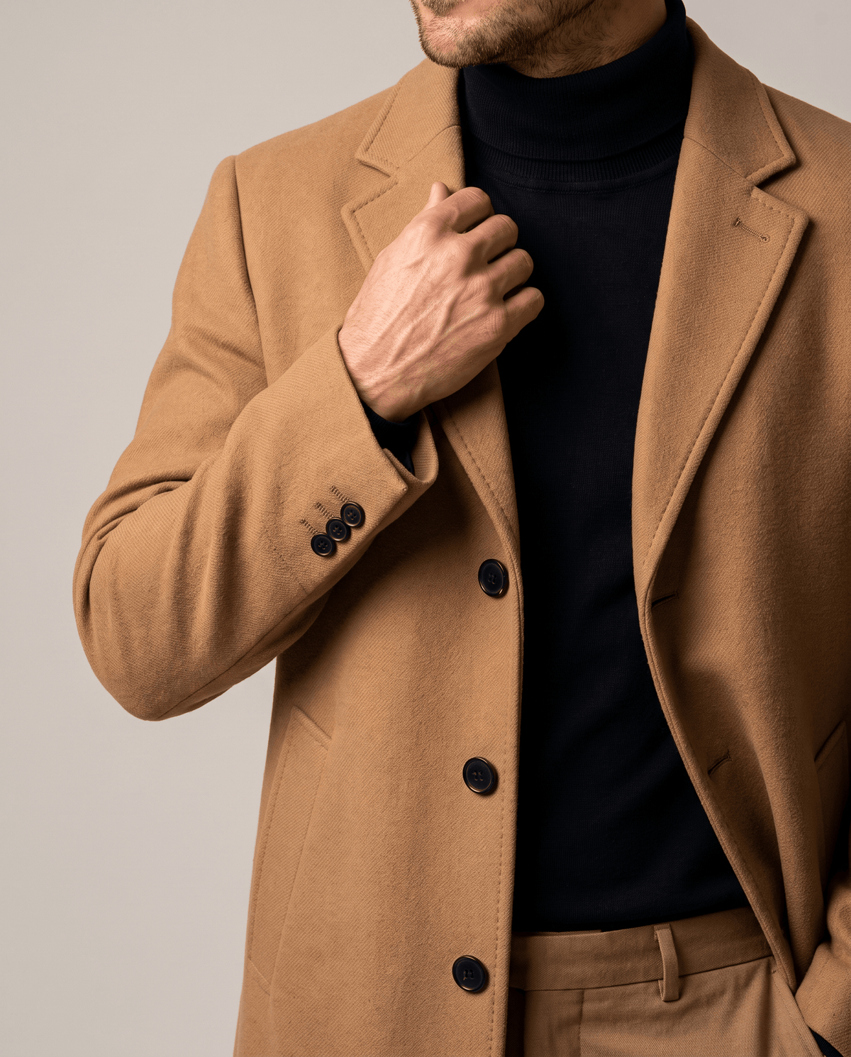 Hand at the collar of the brown coat showing the button row, cuff buttons and slant pocket