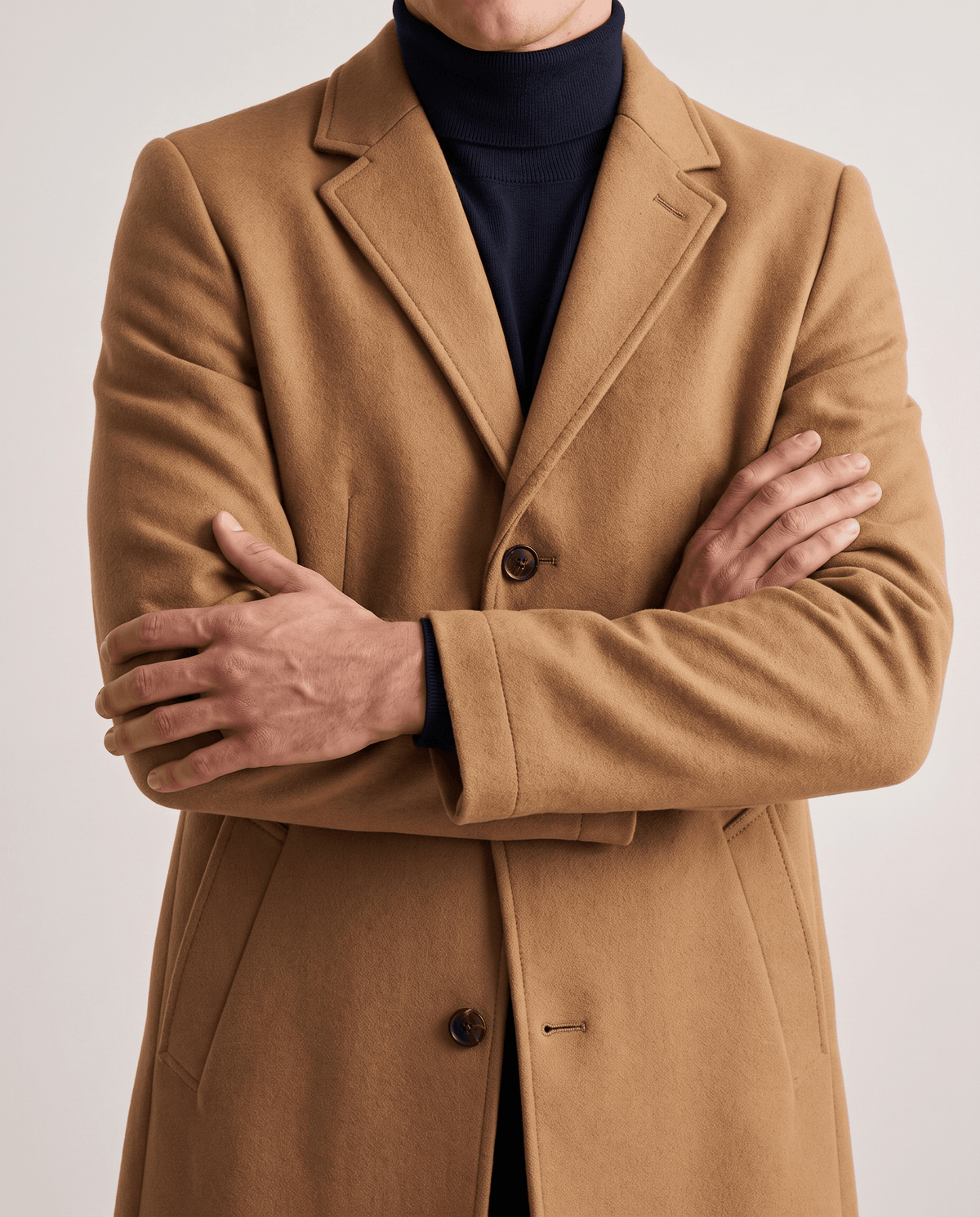 Brown coat close-up with arms crossed over a dark turtleneck, showing lapel and buttons