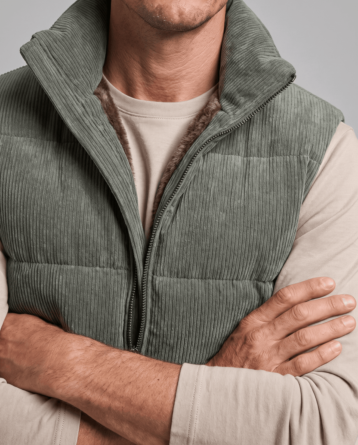Close-up of green corduroy vest with arms crossed, showing quilted panels and stand collar