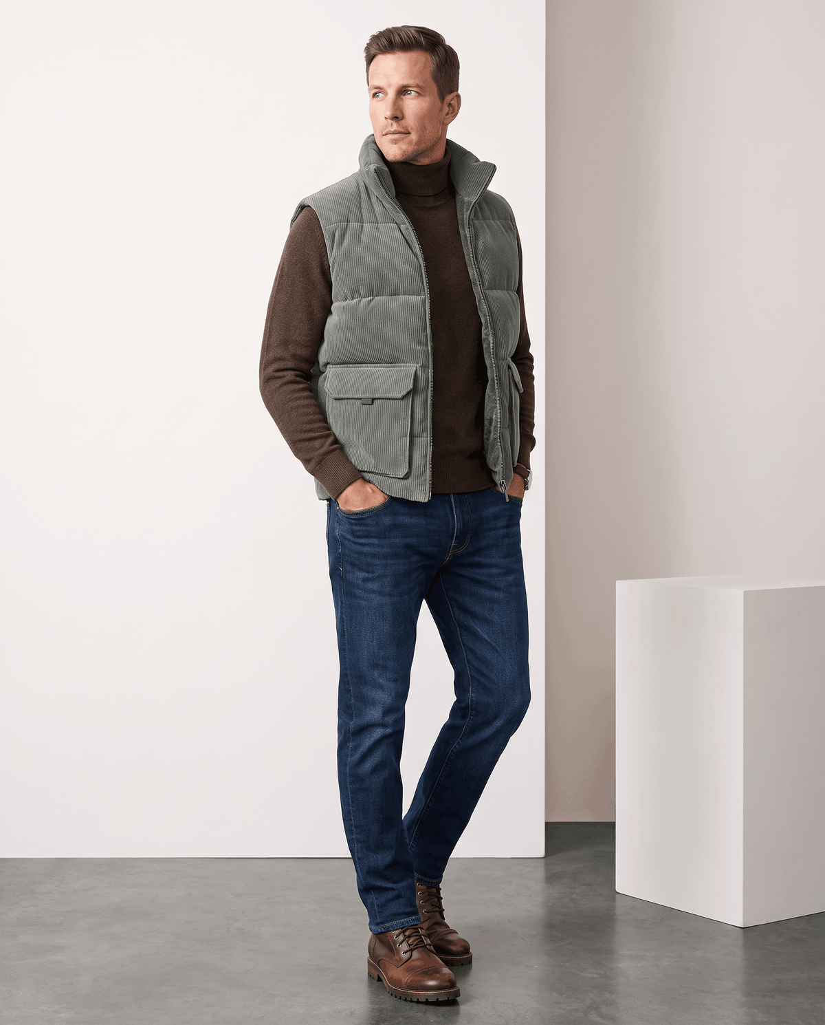 Man in green corduroy vest over a brown sweater with jeans and shoes in studio