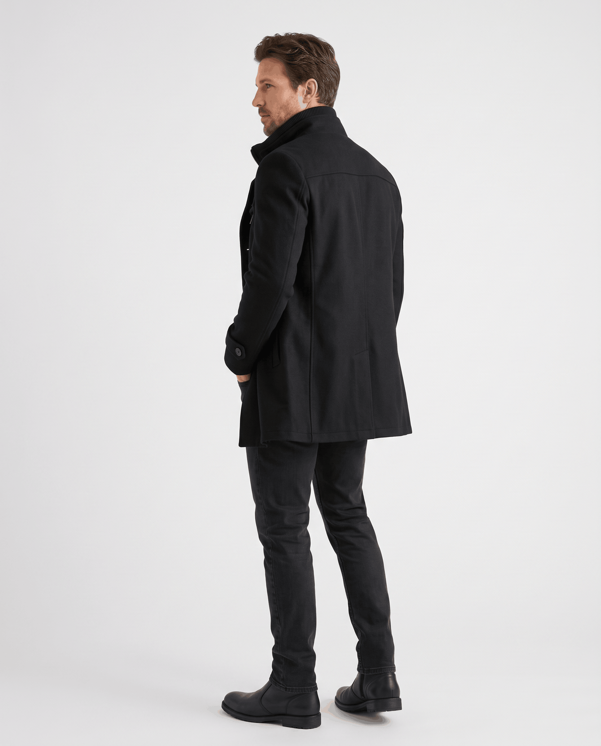 Back view of the black overcoat worn with dark trousers and black boots