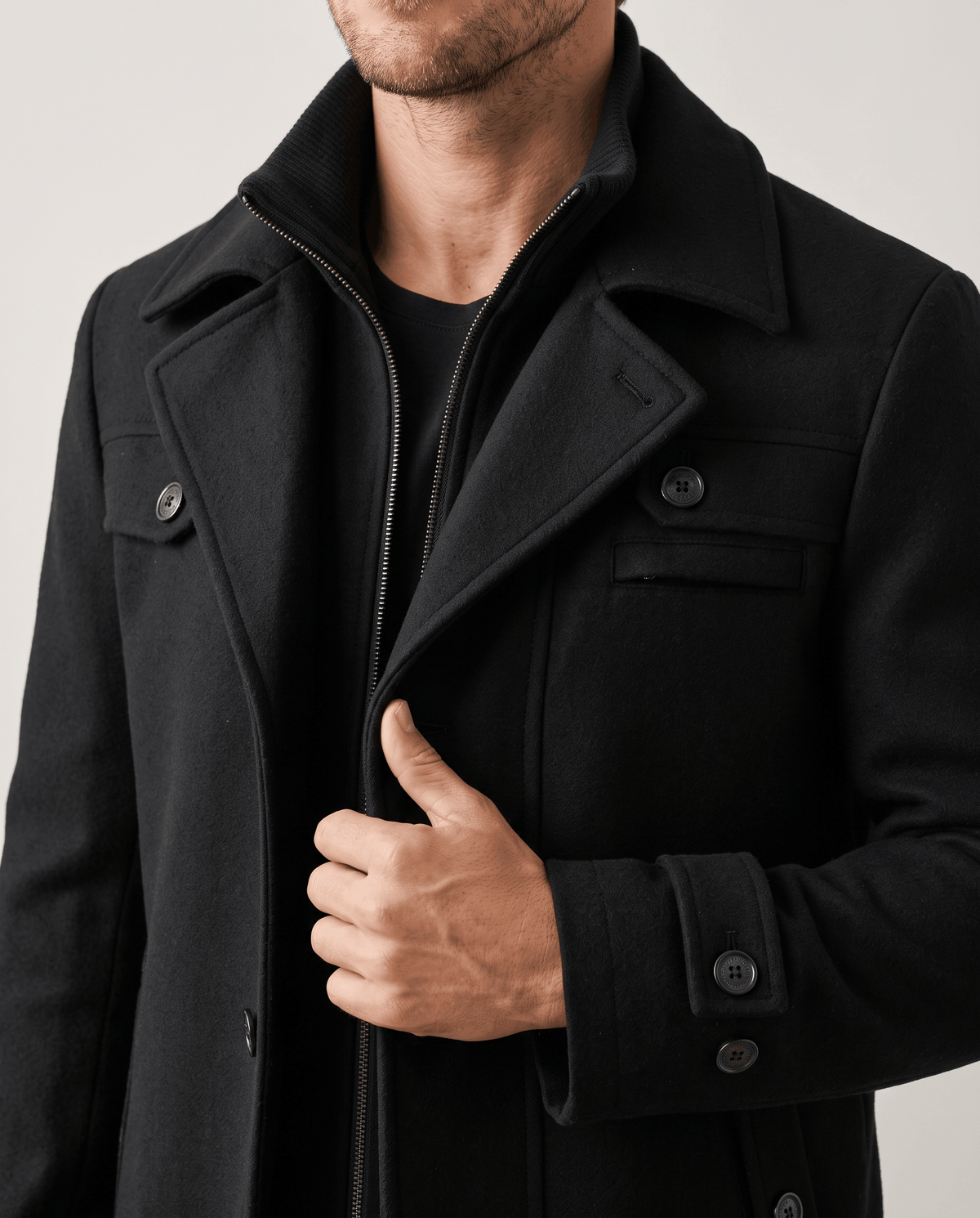 Close-up of the black overcoat's double collar, buttoned chest pocket and button cuff
