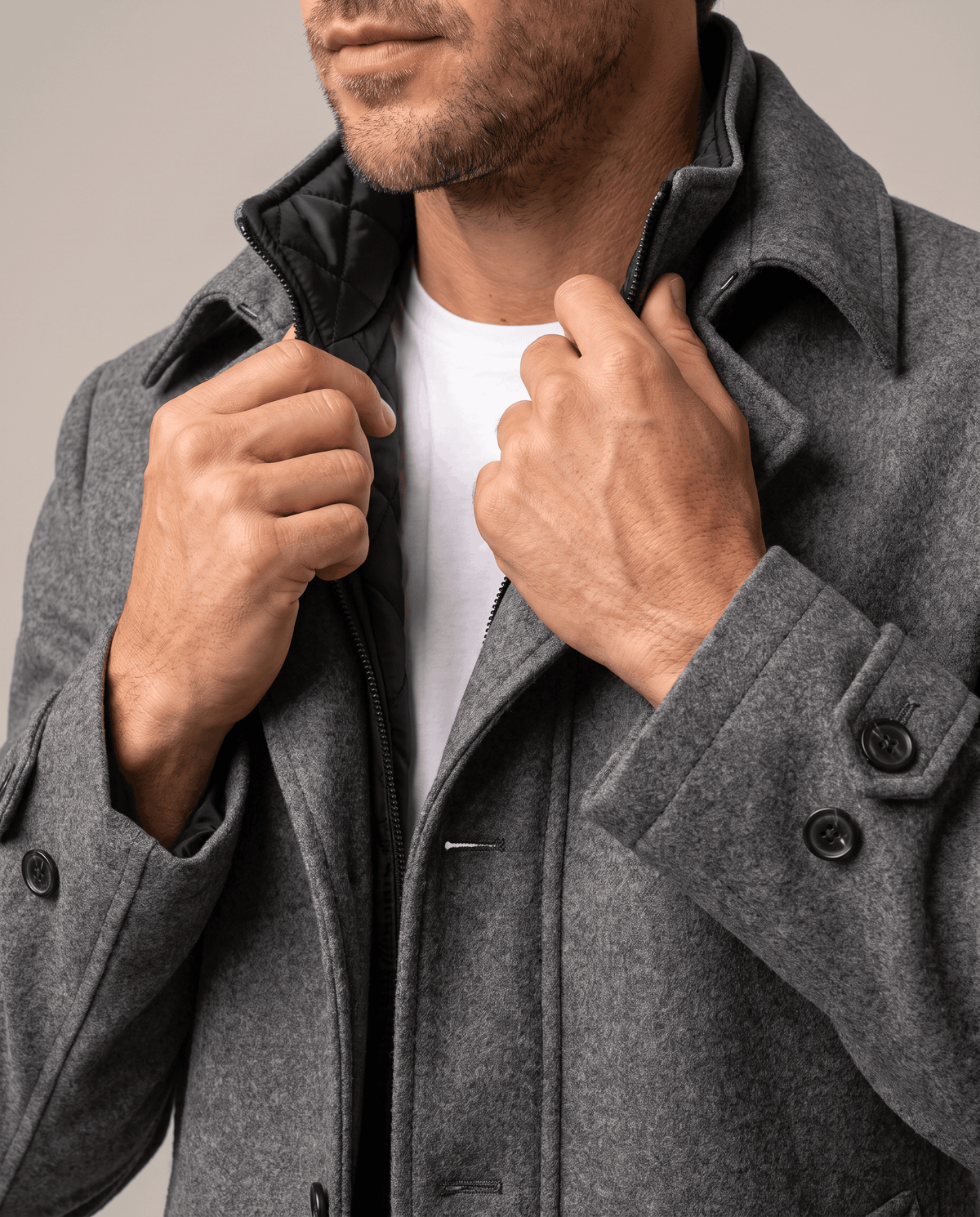 Close-up of the gray overcoat's inner collar and button front, with one hand at the lapel