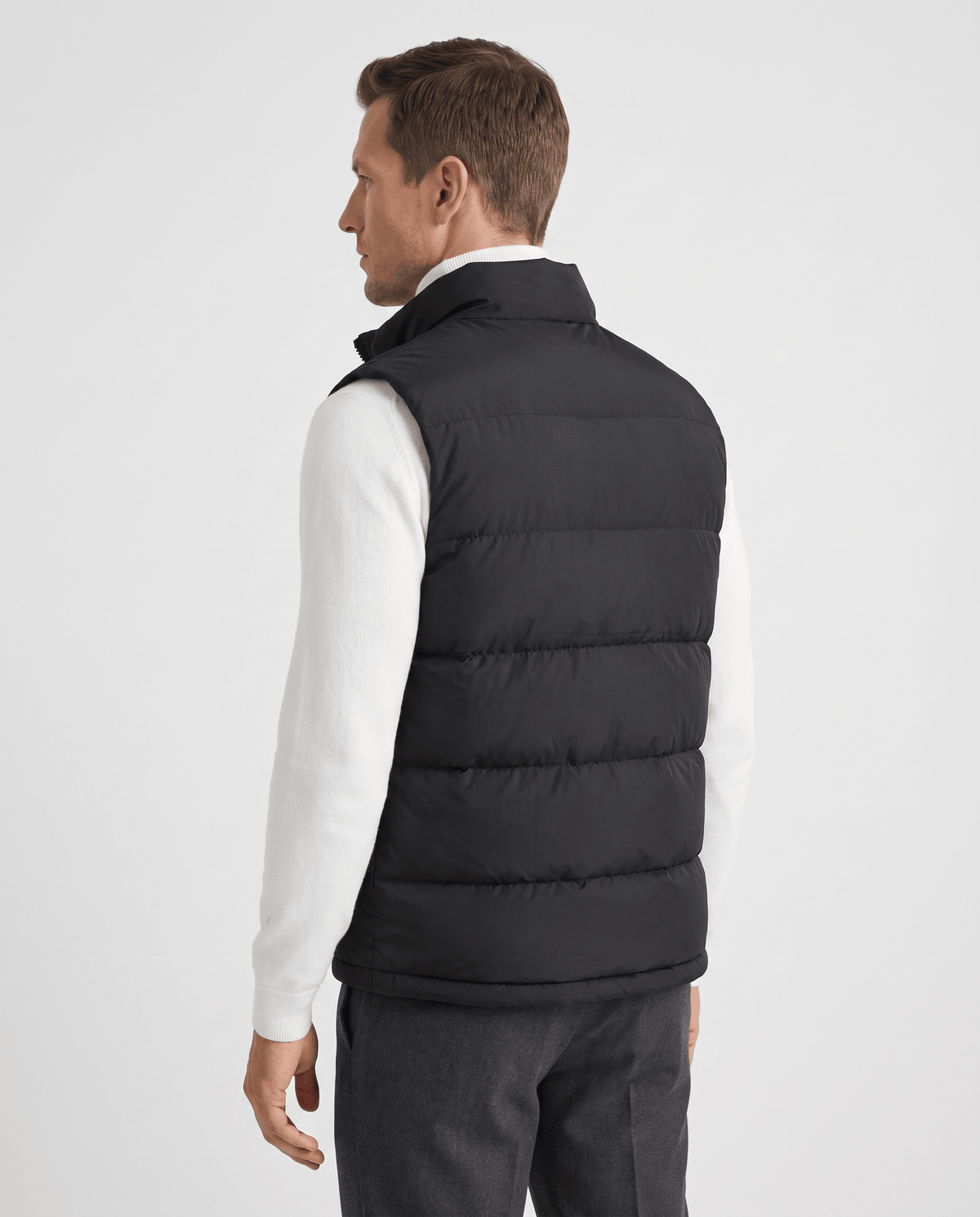 Back view of black quilted vest worn over a white sweater and gray trousers