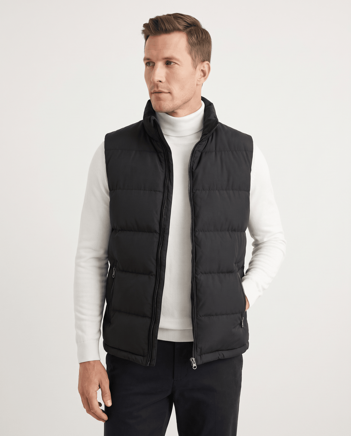 Black quilted vest zipped over a white turtleneck, standing front-on in studio