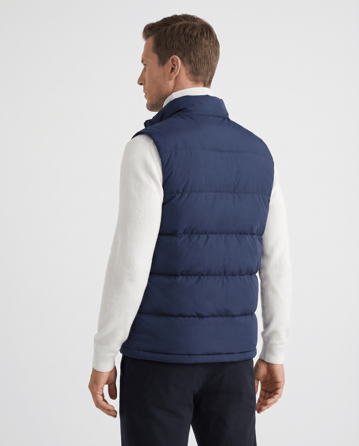 Back view of navy quilted vest worn over a white sweater and dark trousers
