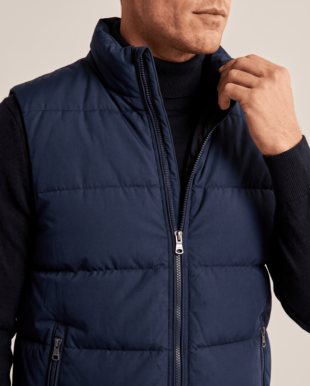 Close-up of navy quilted vest with high collar, front zip and zippered pocket