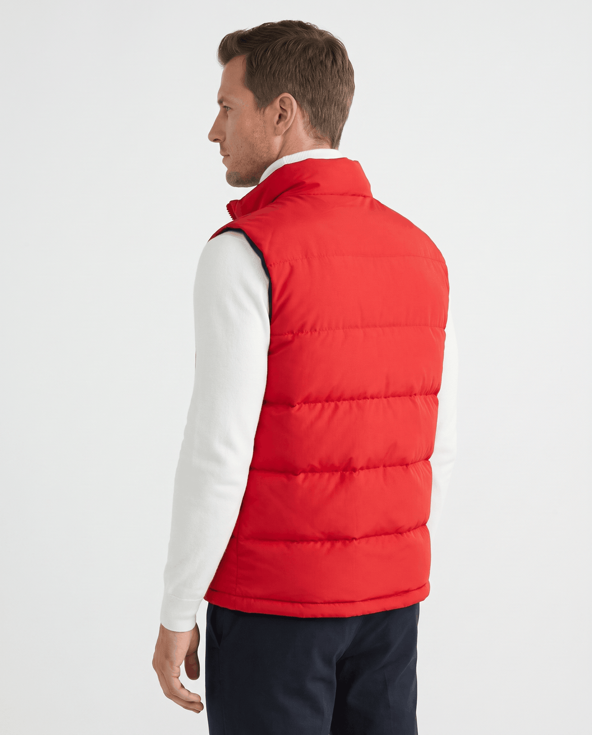 Back view of red quilted vest worn over a white sweater and navy trousers