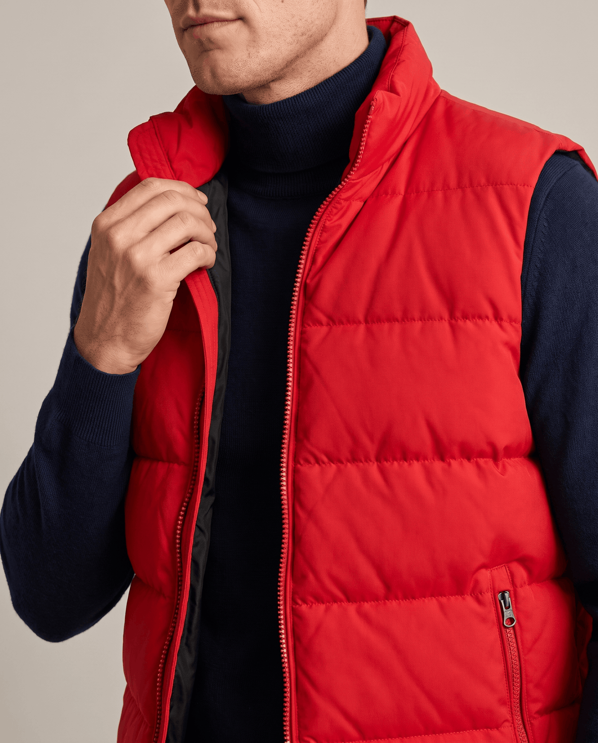Close-up of red quilted vest with front zip and zippered pocket over a navy turtleneck