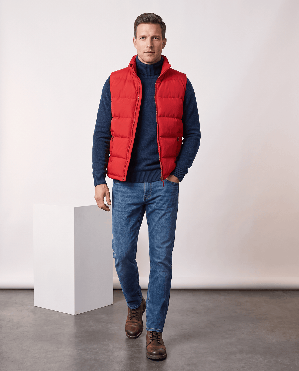 Man in red quilted vest over a navy turtleneck with jeans and brown shoes, full length