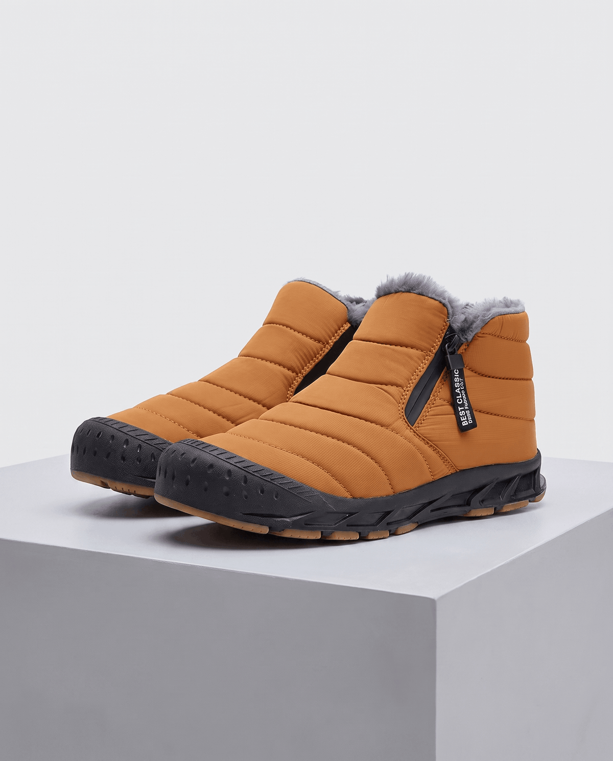 Pair of orange insulated ankle boots displayed on a pedestal.