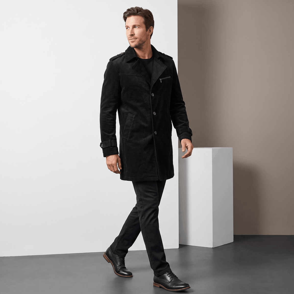 Man wearing a black trench coat in a full-body studio setting.