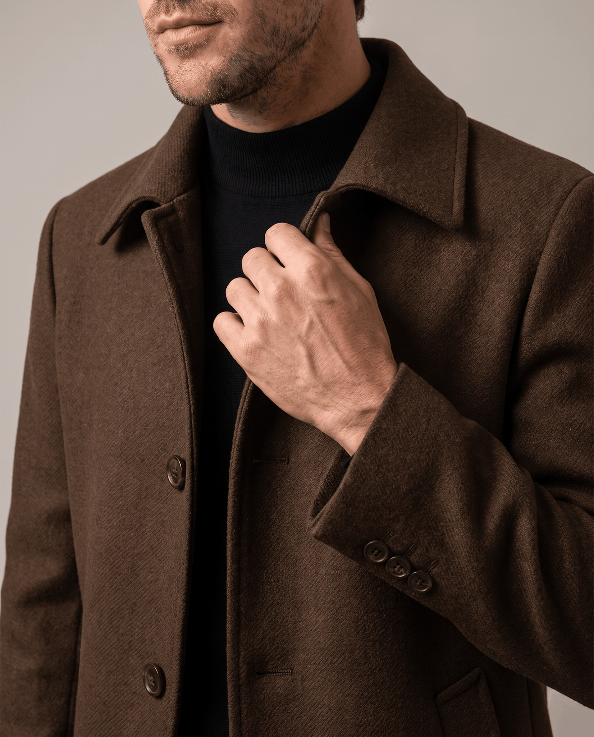 Brown overcoat collar and lapel detail, with one hand at the front opening